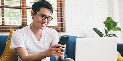 Man on his couch looking at his phone and laptop.